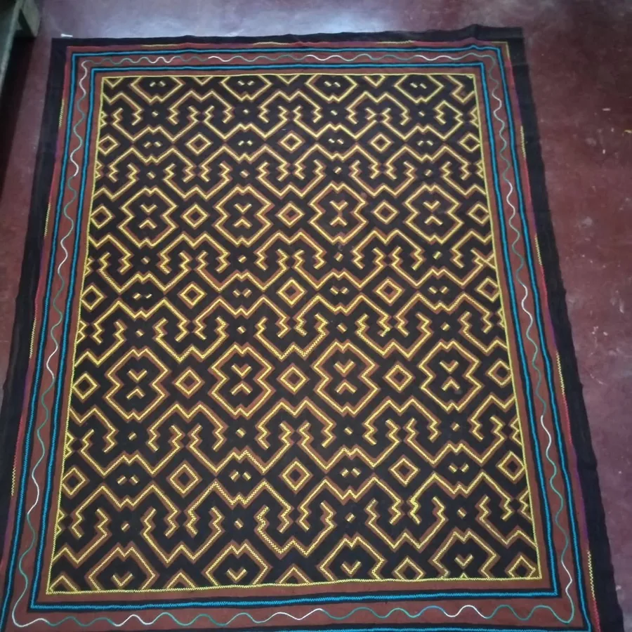 A hand-painted kené cloth: a dense continuous maze of ochre and cream line on a dark ground, bordered on all four sides