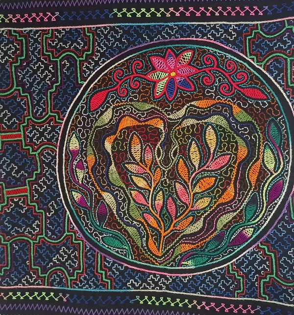 Floral Mandala on Indigo by Simi Vásquez Maldonado: a radial mandala of leaves and blossoms embroidered in many colours, ringed by kené linework on dark indigo cloth