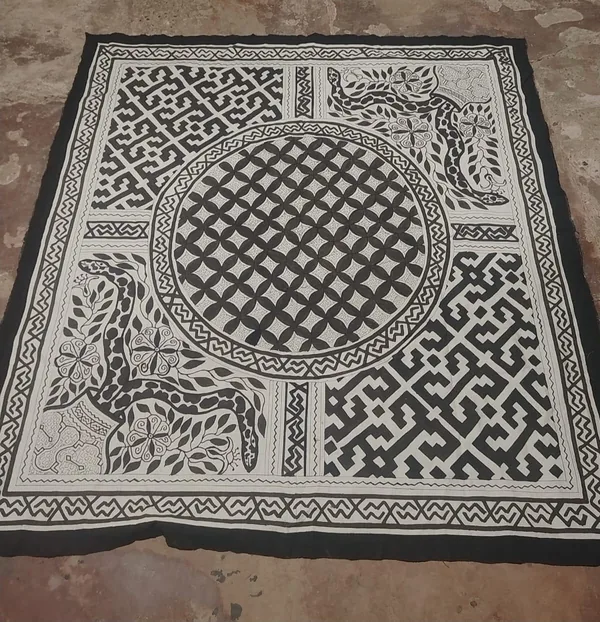 A hand-painted kené cloth in black on natural cloth, a large circular motif at its centre surrounded by geometric field